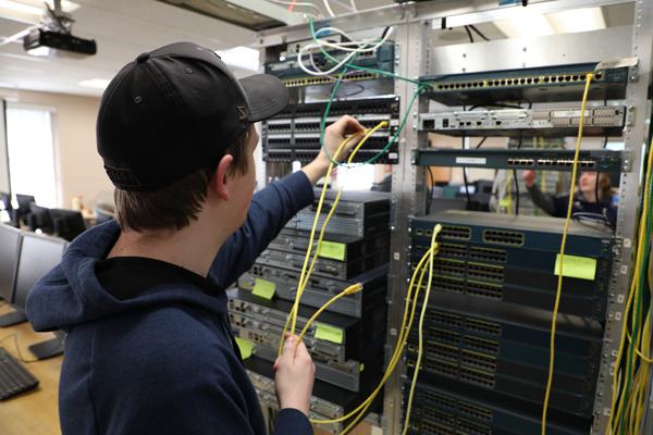 一名男学生将RJ-45电缆插入服务器机架.